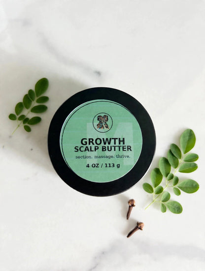 Growth Scalp Butter jar top-down on white marble with moringa sprigs and cloves